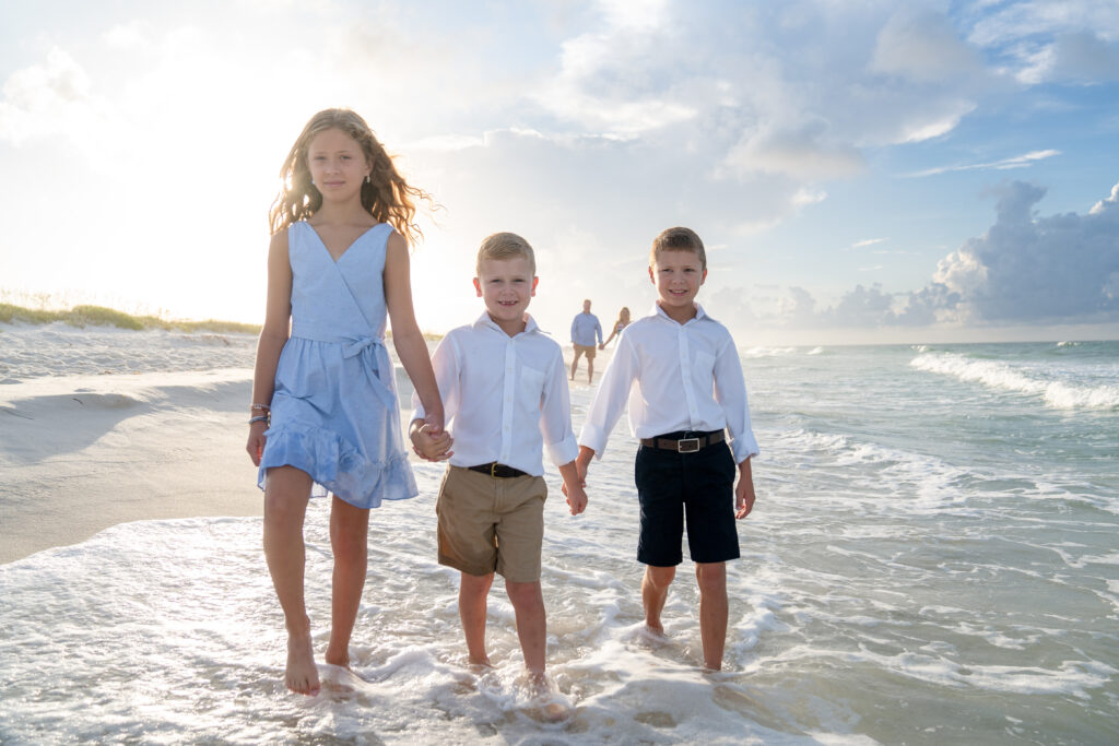 Three children are walking along the beach holding hands.