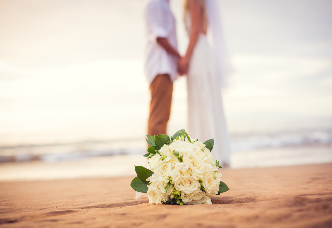 A bouquet of flowers on the beach with two people standing in the background.