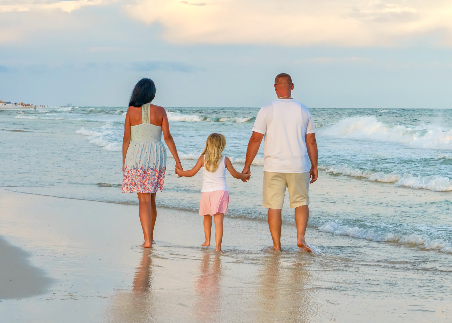A family of three is walking along the beach.