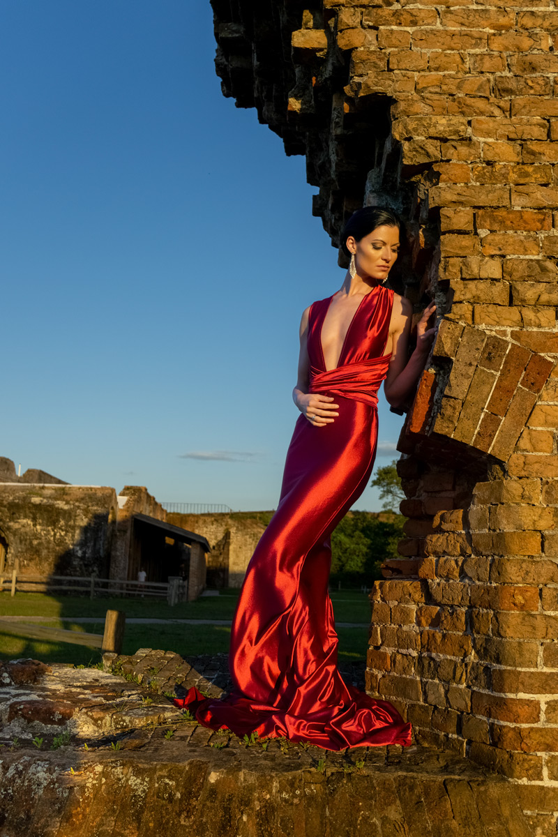 A woman in red dress standing next to brick wall.