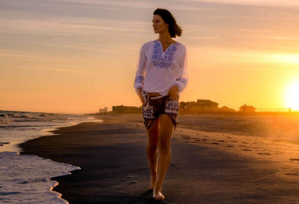 A woman walking on the beach at sunset.