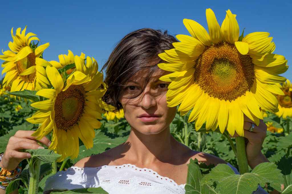 A woman standing in the middle of a field with two sunflowers.