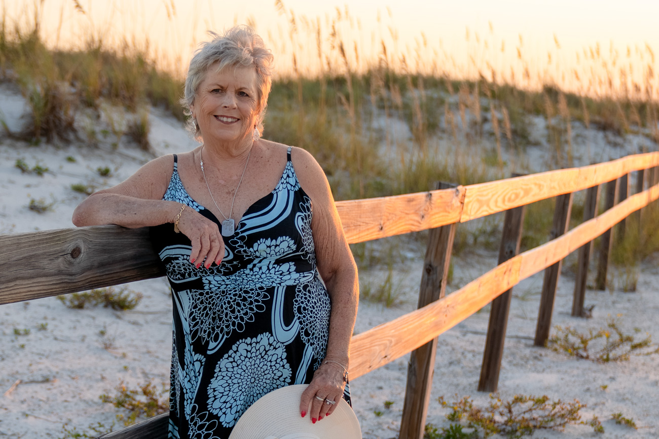 A woman standing next to a fence on the beach.