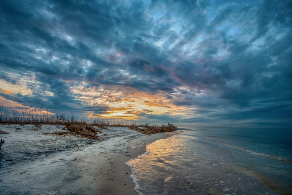 A beach with sand and water under cloudy skies.