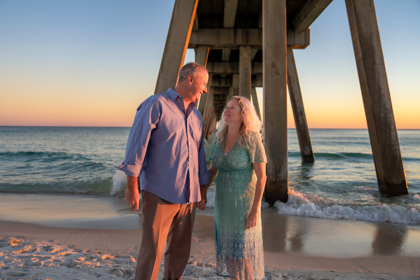 A man and woman standing on the beach under an ocean pier.