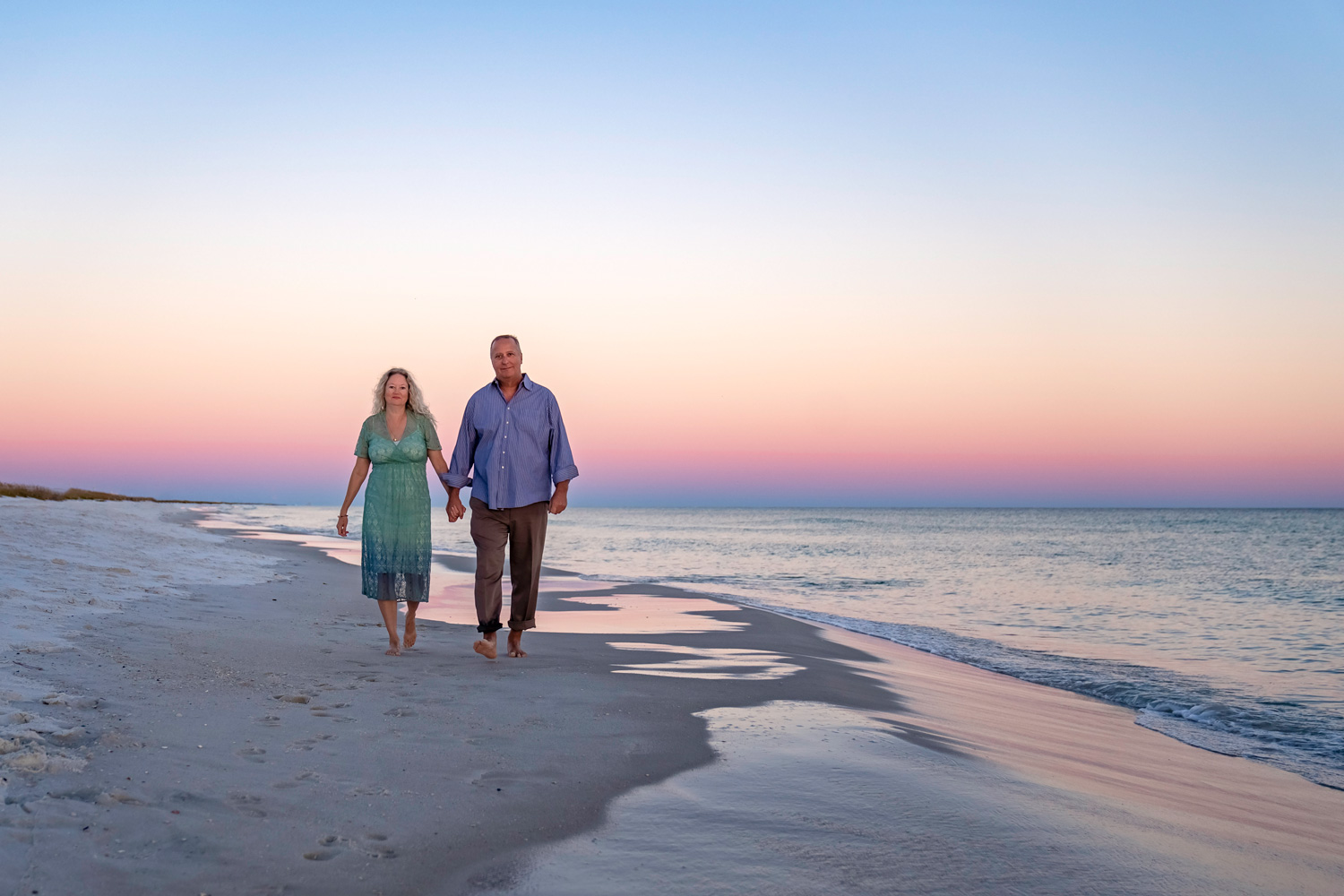 A man and woman walking on the beach at sunset