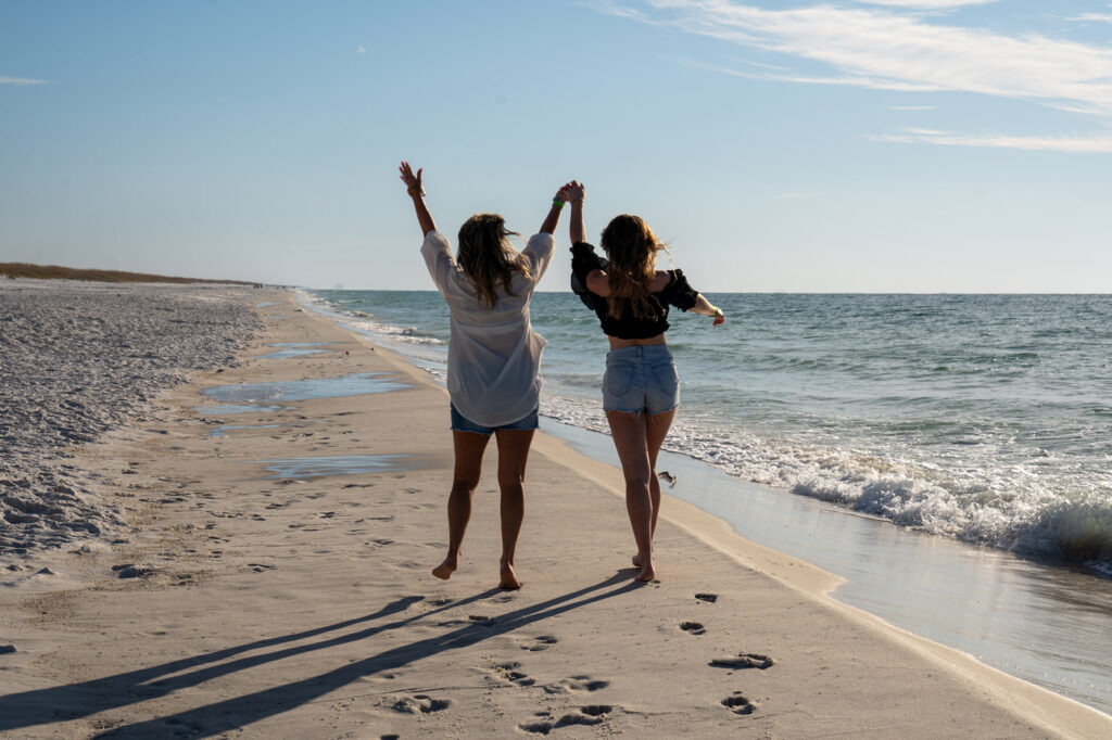 Two women are walking along the beach holding hands.