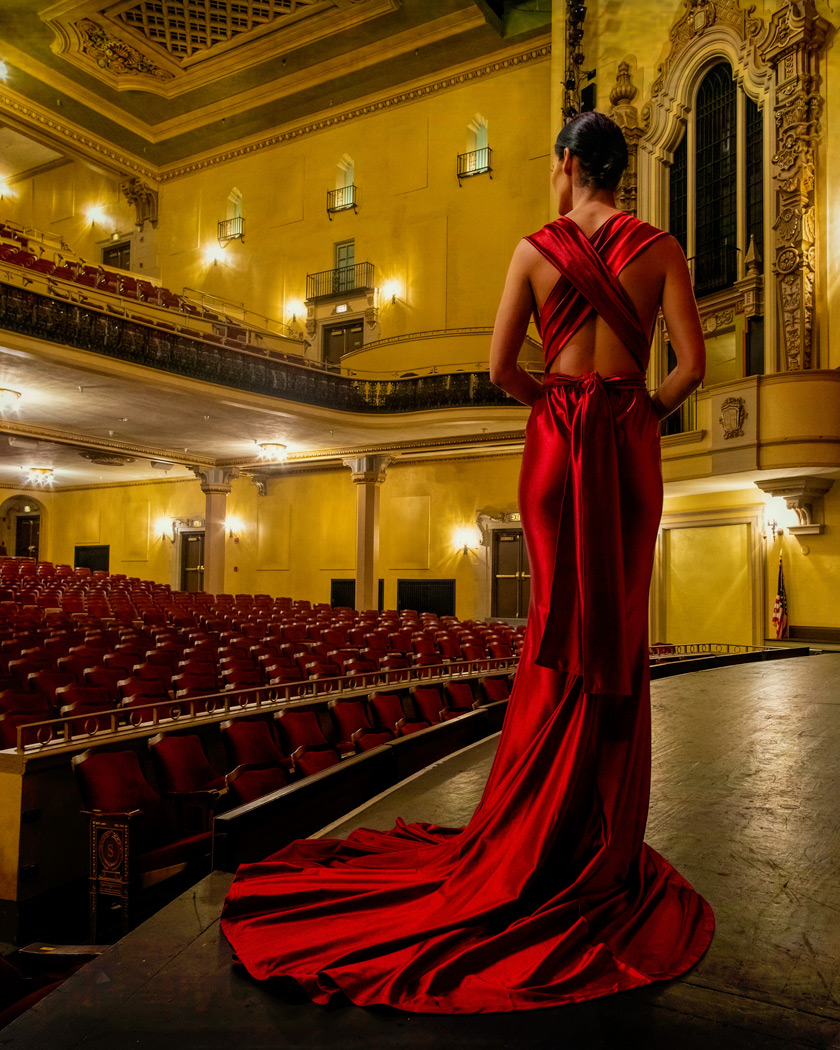 A woman in red dress standing on stage with seats.