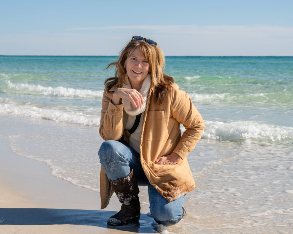 A woman kneeling on the beach in front of the ocean.