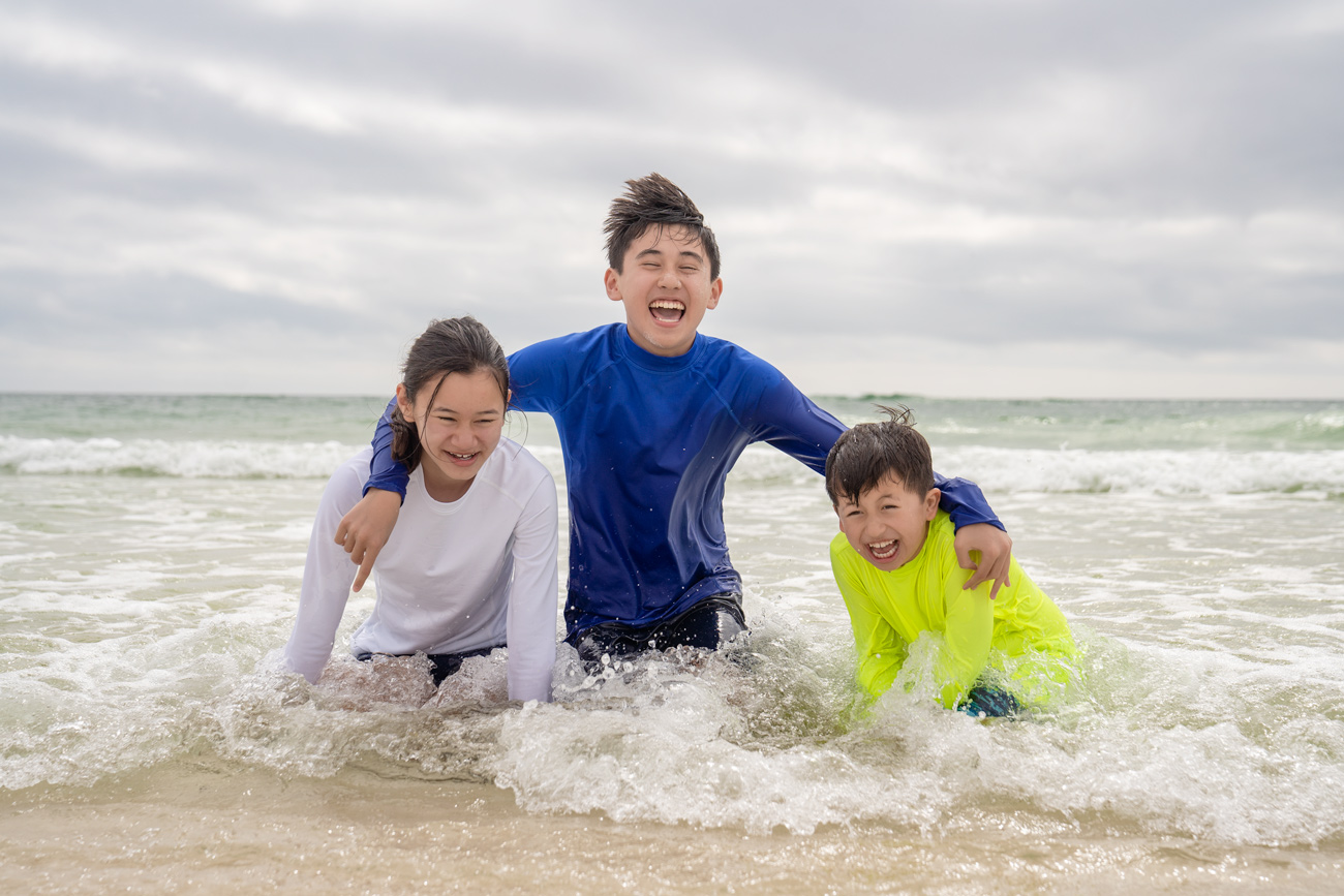 Three children are playing in the water at the beach.